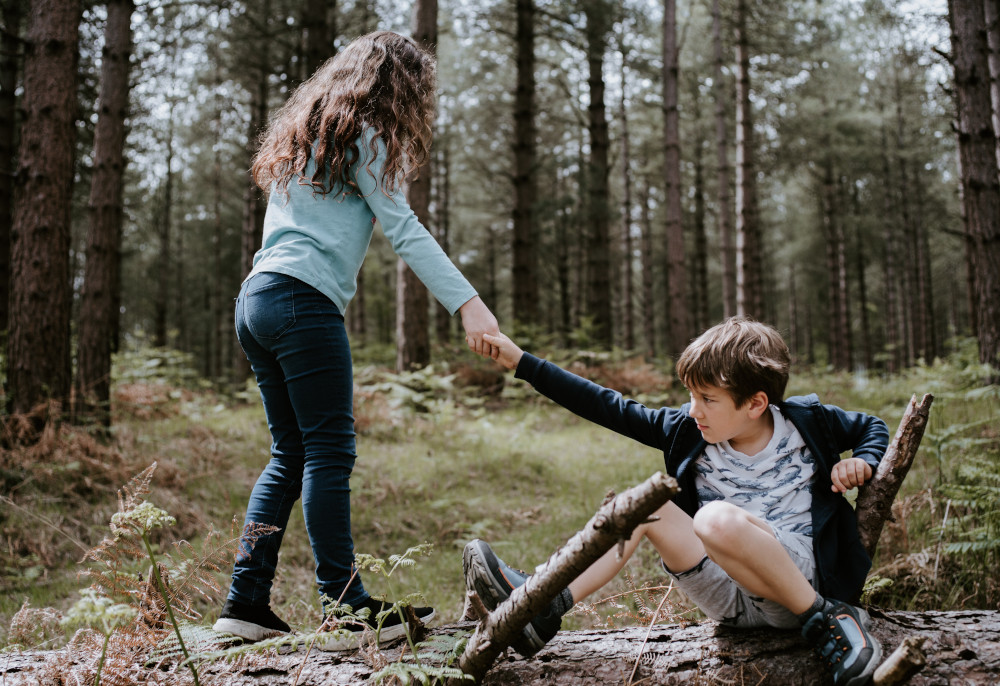 A girl helping a boy in the woods